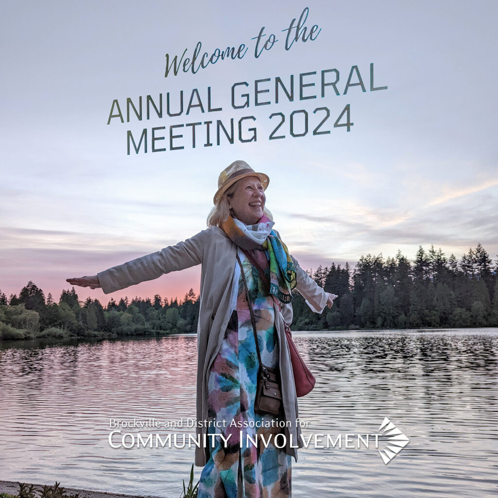 Franke James at Lost Lagoon in Vancouver raises her arms like she is about to take-off. She is wearing the same long, pastel dress as at the BDACI AGM and the type saying, "Welcome to the Annual General Meeting 2024" is superimposed over her. Photo by Billiam James